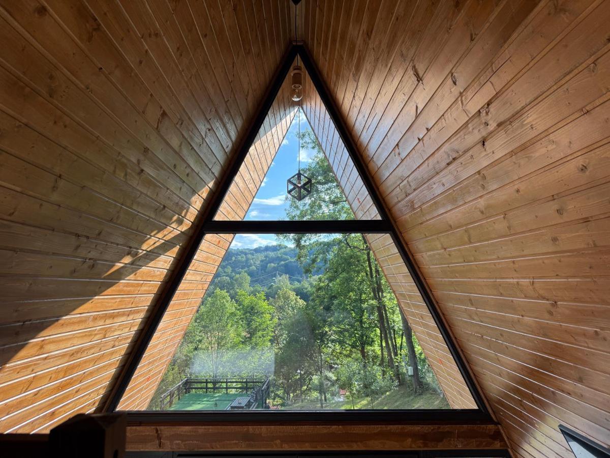 Fereastra triunghiulară a cabanei A-frame, cu pădurea și valea văzute din interior